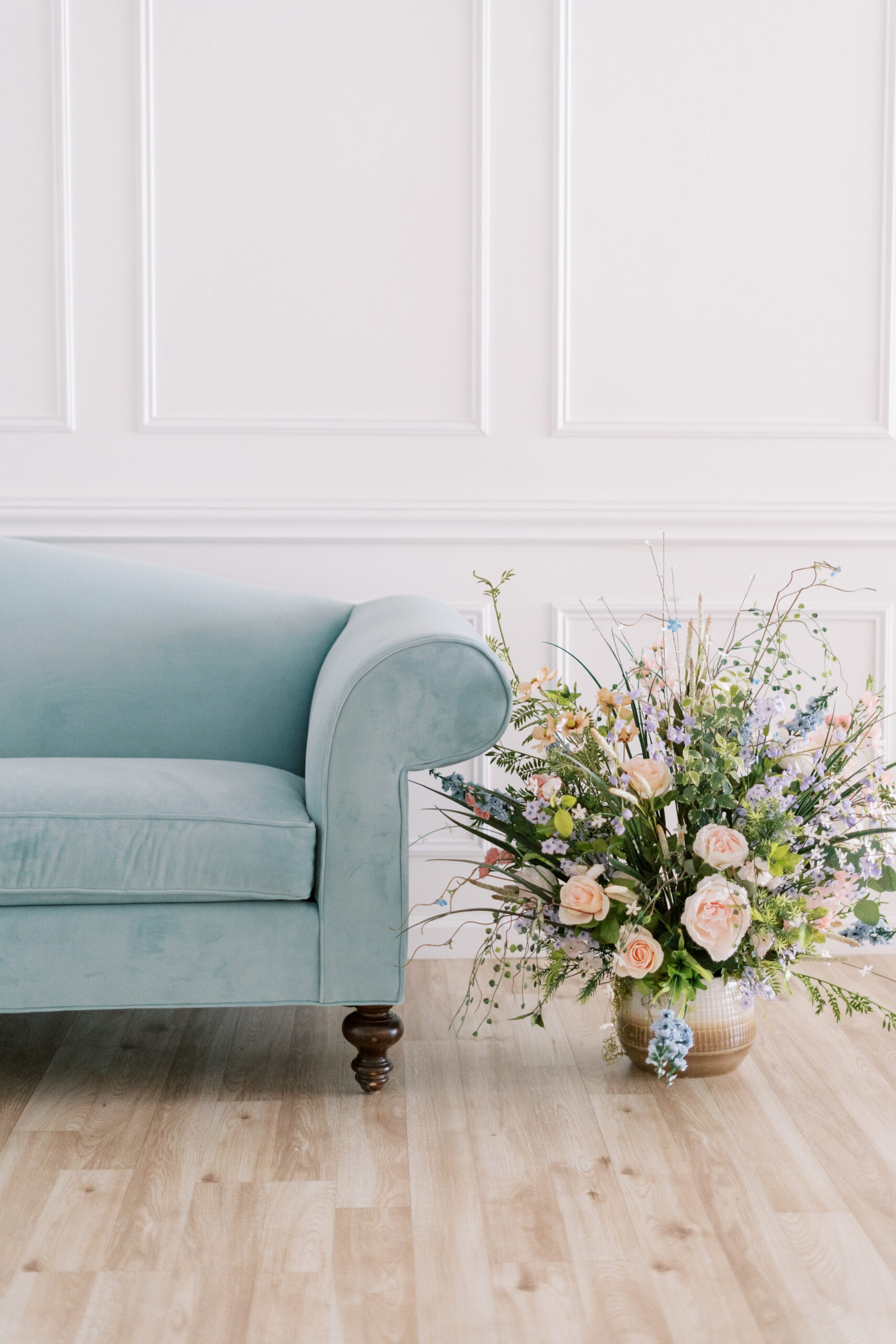 blue velvet couch and pastel flowers in front of accent white wall